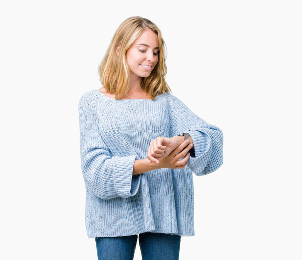 Hermosa mujer joven con suéter azul sobre fondo aislado Comprobación de la hora en el reloj de pulsera, relajado y seguro
 - Foto, imagen