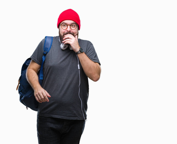 Молодой хипстер в красной шерстяной шапке и рюкзаке на изолированном фоне выглядит напряженным и нервным с руками во рту, грызущими ногти. Проблема тревоги
. - Фото, изображение