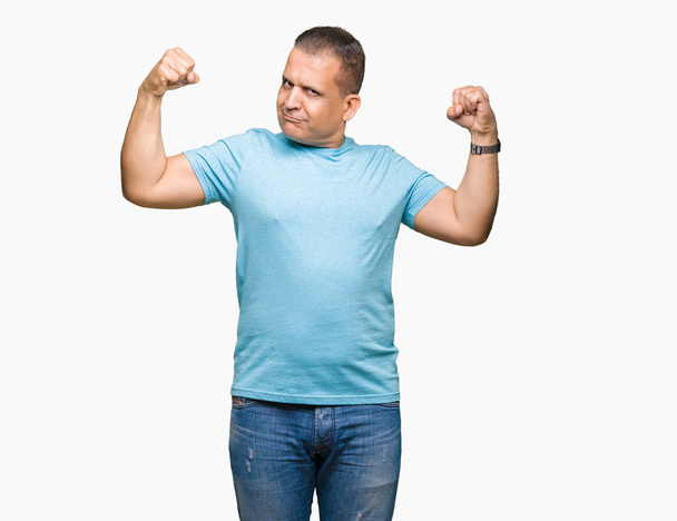 Homme arabe du Moyen Age portant un t-shirt bleu sur fond isolé montrant les muscles des bras souriant fier. Concept de fitness
. - Photo, image