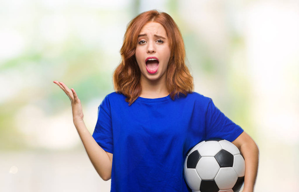 Молодая красивая женщина на изолированном фоне, держа футбольный мяч очень счастлив и взволнован, победитель выражение празднования победы кричать с большой улыбкой и поднятые руки
 - Фото, изображение