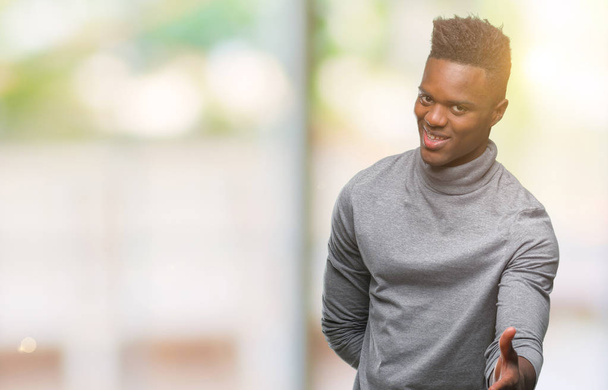 Молодий афроамериканець людиною над ізольованих фону, посміхаючись дружні пропонуючи рукостискання як привітання і вітаючи. Успішний бізнес. - Фото, зображення