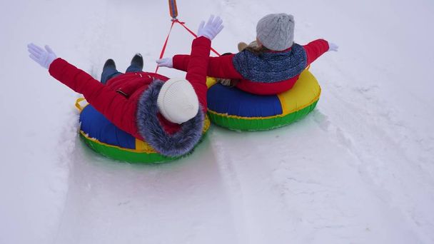 kinderen in rode jassen rit door sneeuw in de winter op een opblaasbare sneeuw pijp en spelen super helden. Gelukkig meisjes ontspannen in de winter park voor de kerstvakantie. Slow motion - Foto, afbeelding