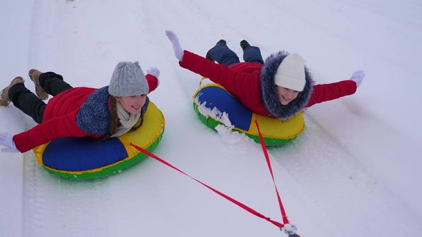 Дівчата в червоних куртках їздять по снігу взимку на надувній сніговій трубі і грають супергероїв. щасливі дівчата відпочивають у зимовому парку на різдвяні свята. Повільний рух
 - Фото, зображення