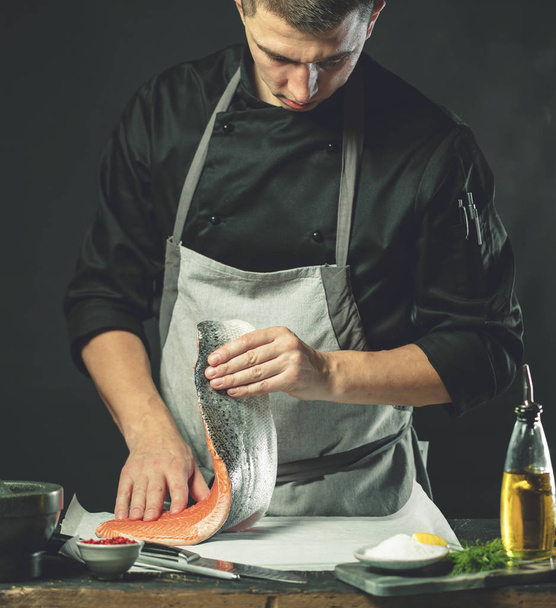 The big salmon is in the hands of the chef cook. He is using a knife to slice salmon fillet - Foto, imagen