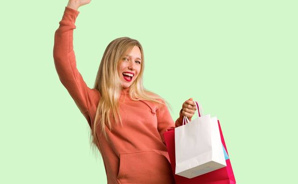 junges Mädchen mit vielen Einkaufstüten in Siegerpose auf grünem Hintergrund - Foto, Bild