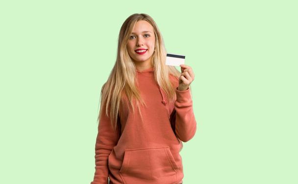 Young girl holding a credit card on green background - Fotoğraf, Görsel