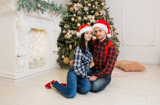 genç kişi yakınındaki Noel ağacı Noel şenlikli elbiseli kız arkadaşı ile güzel ve şömine hediyeler ile şenlikli ruh hali sunar. - Fotoğraf, Görsel