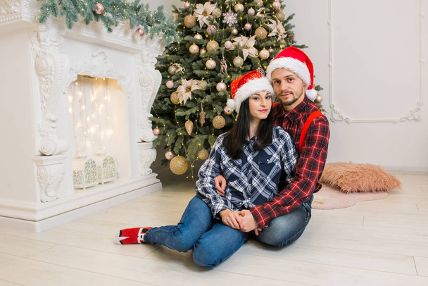 молода красива людина з дівчиною в різдвяній святковій сукні біля ялинки та каміна подарунки зі святковим настроєм
 - Фото, зображення