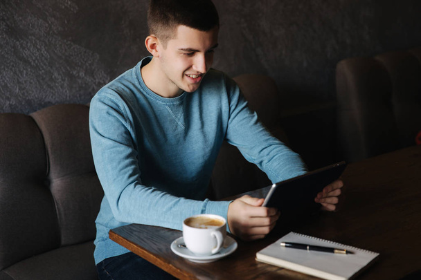 Ο άνθρωπος κάθεται σε μια καφετέρια και χρησιμοποιώντας ένα tablet. Μαθητής περνούν χρόνο σε καφέ και καφέ. Αυτός μελετήσει και σημειώστε χρήσιμες πληροφορίες - Φωτογραφία, εικόνα