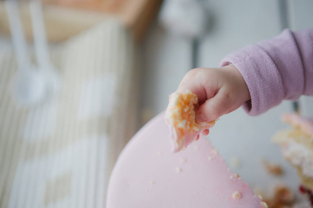 child holds a pink cake slice a small hand - Zdjęcie, obraz