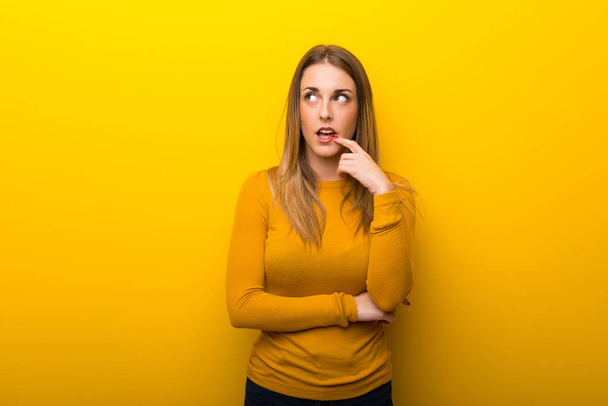 Young woman on yellow background having doubts while looking up - Photo, Image