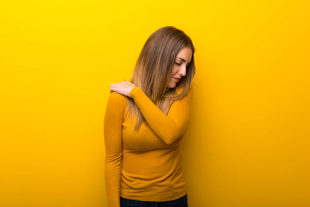 Jonge vrouw op gele achtergrond lijden aan pijn in schouder voor een inspanning hebben gedaan - Foto, afbeelding