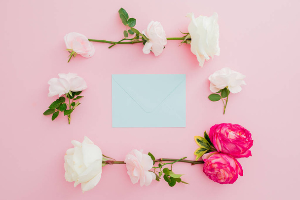 Floral frame with roses flowers and blue envelope on pink background. Flat lay, top view. Valentines day - Photo, Image