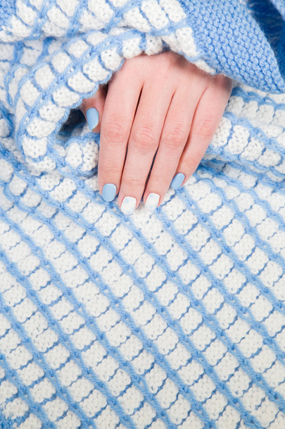 Closeup view of painted blue and white fingernails of young woman isolated on cozy warm blanket. Winter style of manicure. Horizontal color photography. - Photo, Image