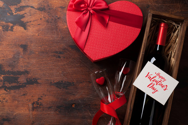 Открытка на день Святого Валентина с бутылкой красного вина и коробкой подарков любви на деревянном фоне. Вид сверху с местом для приветствия. Плоский лежал
 - Фото, изображение
