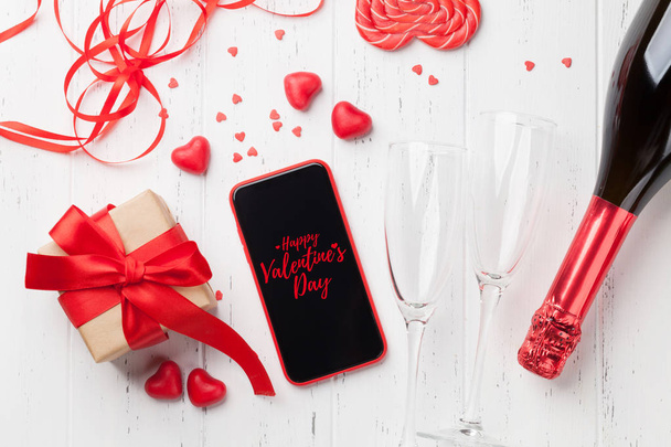 Открытка на день Святого Валентина с подарочной коробкой, шампанским и смартфоном на деревянном фоне. Вид сверху с местом для приветствия или приложения для смартфона. Плоский лежал
 - Фото, изображение
