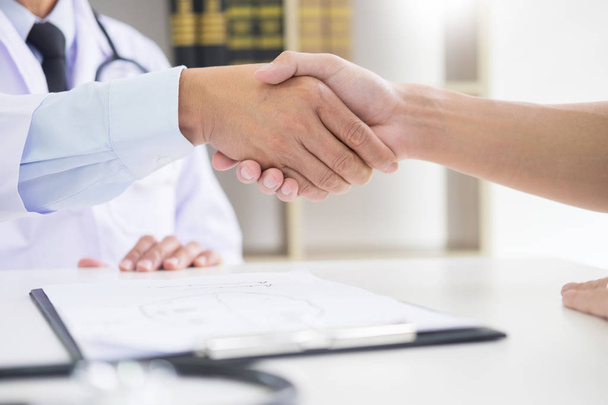 doctor at the clinic giving an handshake to his patient for encouragement and empathy, healthcare and assistance concept - Photo, image