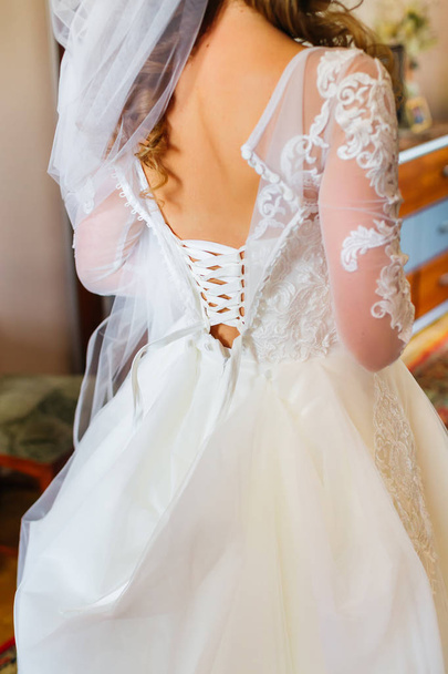 the bride is standing back to the camera in bridal veil and wedding gown. the dress is unbuttoned on the back and visible to the birthmark - Photo, Image
