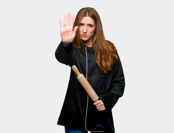 Joven pelirroja chef mujer haciendo stop gesture negando una situación que piensa mal sobre fondo gris aislado
 - Foto, Imagen