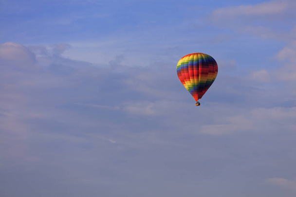 A motley multicolored beautiful balloon raises the tourist's basket to the blue sky under the sun rays among the clouds. - Photo, Image