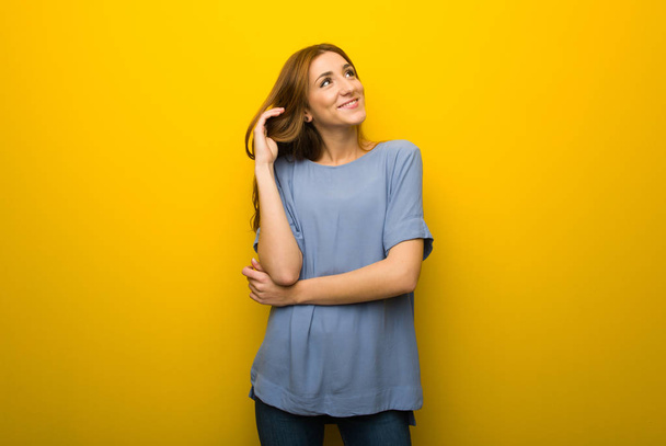 Young redhead girl over yellow wall background thinking an idea while scratching head - Foto, Bild