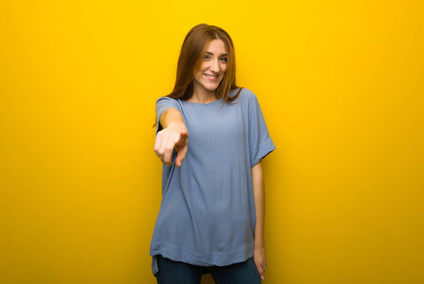 Jeune fille rousse sur fond mural jaune pointe du doigt vers vous avec une expression confiante
 - Photo, image
