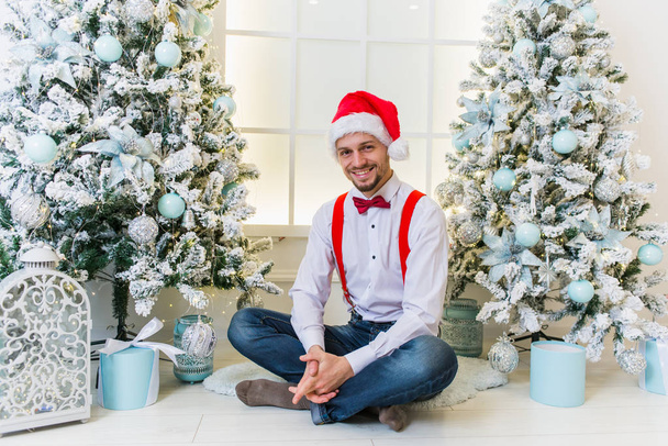 a man with a beard in a festive dress with red tights of jeans and a cloth shirt near a fir tree - Photo, Image