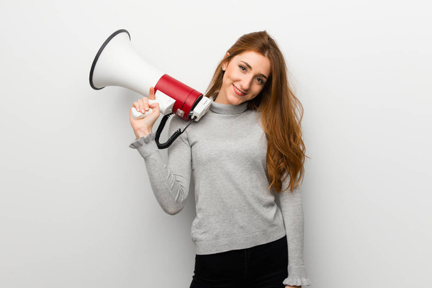 Redhead girl over white wall holding a megaphone - Foto, afbeelding