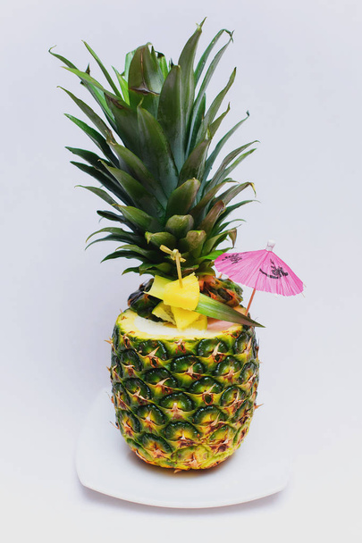Heerlijke dessert van ananas. Ananas Cocktail exotisch fruit ingericht met een cocktail paraplu en fruit plakjes. Heerlijke traktatie van ananas op een witte plaat. Voedsel voor restaurant en binnenlandse. - Foto, afbeelding