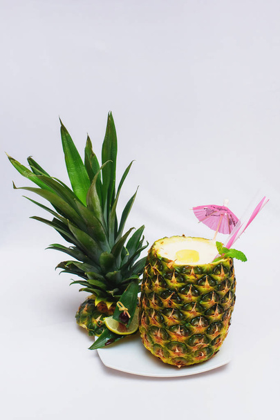 Exquisite dessert from pineapple. Pineapple Cocktail Exotic fruit decorated with a cocktail umbrella and fruit slices. Delicious treat of pineapple on a white plate. Food for restaurant and home. - 写真・画像