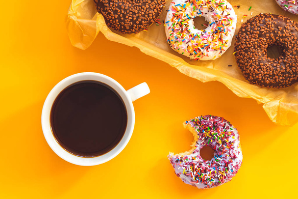 Delicious glazed donuts in box and cup of coffee on yellow surface. Flat lay minimalist food art background. Top view. - Photo, Image