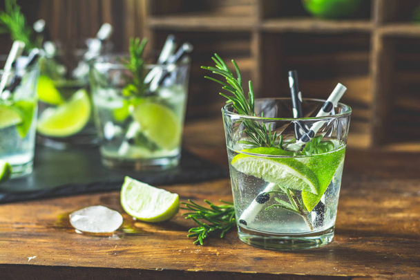 Cocktail frais avec citron vert, glace et romarin, cocktail de mojito dans un bourdonnement sur une table rustique, mise au point sélective, faible profondeur du champ
. - Photo, image