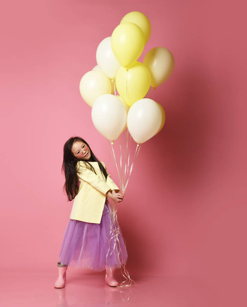 Little Korean baby girl in yellow fashion jacket and purple dress with balloons celebrate happy smiling - Photo, Image