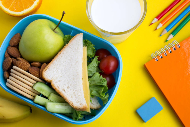 School lunch in the box, milk in the glass and notebook on the yellow background.Top view. - Foto, Bild