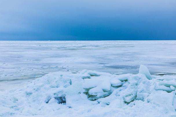 The winter gulf of the sea covered with snow and ice. White and blue beautiful landscape with cloudy sky, white surface of the sea and the heap of floes on the shore - Foto, immagini