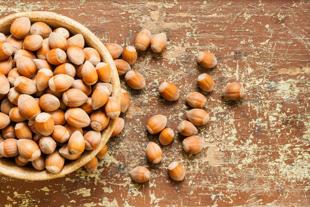 Organic ripe hazelnuts in clay bowl on a wooden table - Фото, изображение