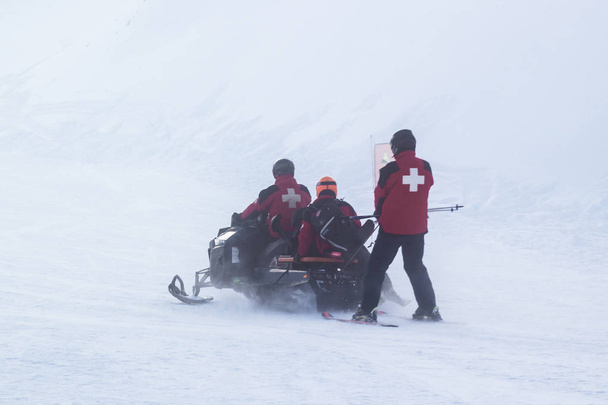 El salvavidas viaja en moto de nieve por las montañas. trabajador médico, trabajador de salud, profesional de la salud, profesional médico, profesional de la salud, trabajador de la salud
. - Foto, imagen