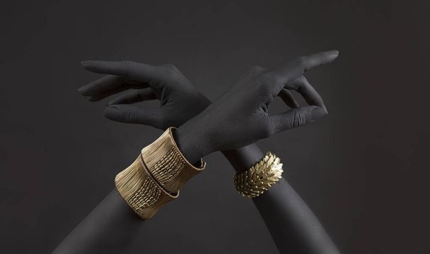 Black woman's hands with gold jewelry. Oriental Bracelets on a black painted hand. Gold Jewelry and luxury accessories on black background closeup. High Fashion art concept  - Photo, Image