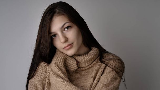 ライトグレーの背景に暖かいニットのセーターの豪華な若いブルネットの女性 - 写真・画像