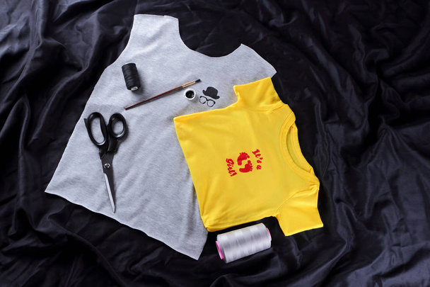 Sewing of children's t-shirts with handmade drawing. Gray and yellow fabric on a dark background. Process of tailoring. Gray and yellow fabric with pictures. Blanks for t-shirts on a black background - Фото, зображення