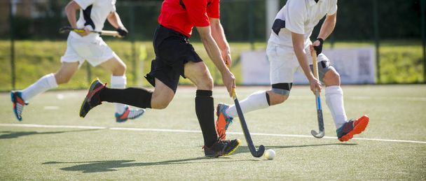 Close up of three field hockey players, challenging eachother for the control and posession of the ball during an intense, competitive match on professional level - Foto, imagen
