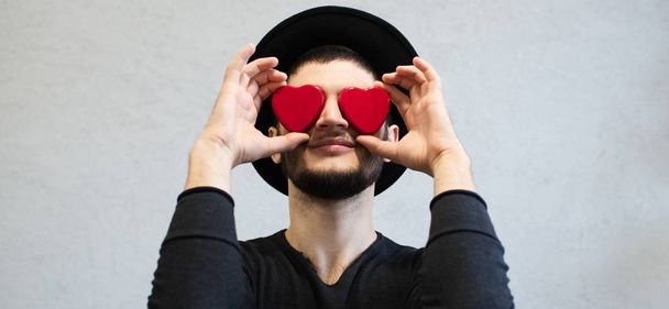 Smiling young man holding red hearts on eyes - Valokuva, kuva