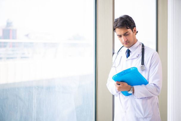 Молодой красивый доктор стоит у окна
  - Фото, изображение