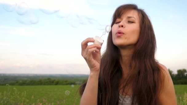 Mladá dívka foukání transparentní mýdlové bubliny proti modré obloze a směje se. Zpomalený pohyb. - Záběry, video