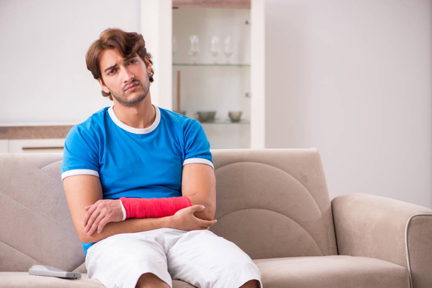 Young man with injured arm sitting on the sofa  - Photo, Image