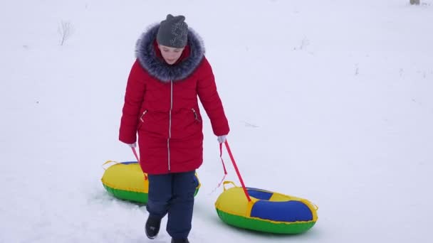 Teen girl climbs high snowy mountain holding two snow saucer. Christmas Holidays - Footage, Video