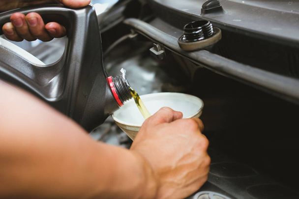 mechanic pouring oil to vehicle engine. serviceman changing motor oil in automobile repair service. maintenance and checkup in car garage - Photo, Image