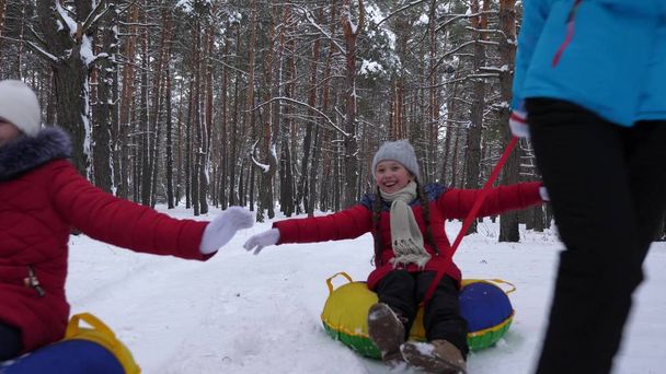onnellinen isä ja äiti vetävät kelkat lasten kanssa talvimetsässä. vanhemmat leikkivät lasten kanssa lumisessa puistossa talvella. onnellista perheen kelkkailua joululomien aikana
. - Valokuva, kuva