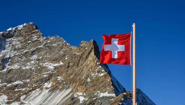 Jungfrau (İsviçre), kar tepe ve mavi gökyüzü arka plan zirvesine karşı İsviçre bayrağı. - Fotoğraf, Görsel
