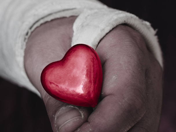 Mužských ruku v sádře obsazení drží malé lesklé červené srdce. - Fotografie, Obrázek